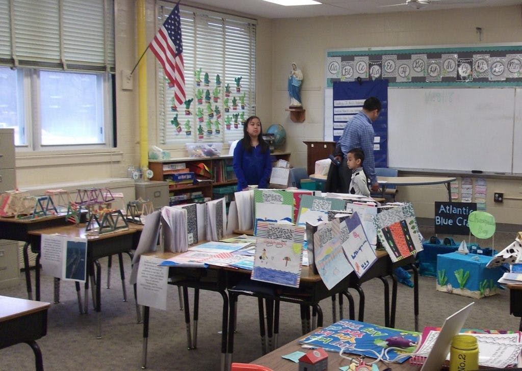 People in a classroom with desks covered in papers and projects