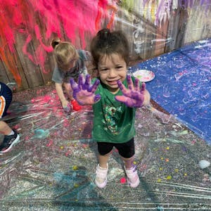 Child with purple paint on hands, smiling at camera