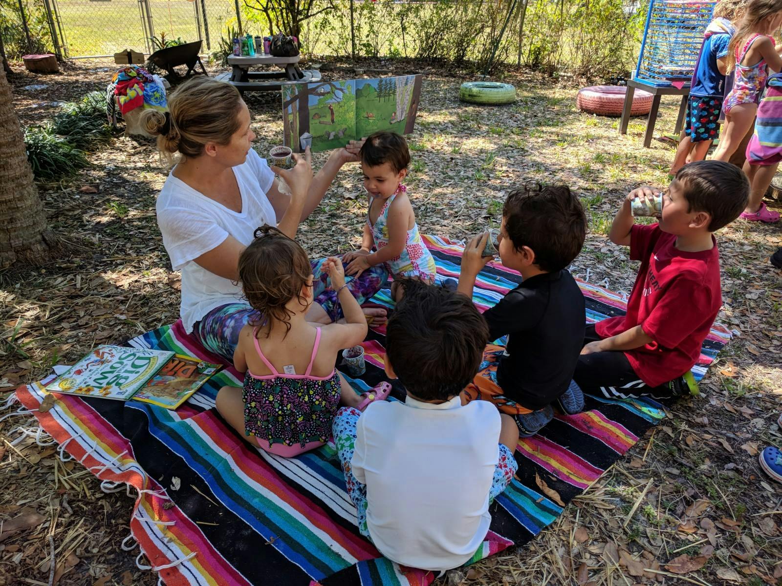 Person sitting on blanket with several children outdoors
