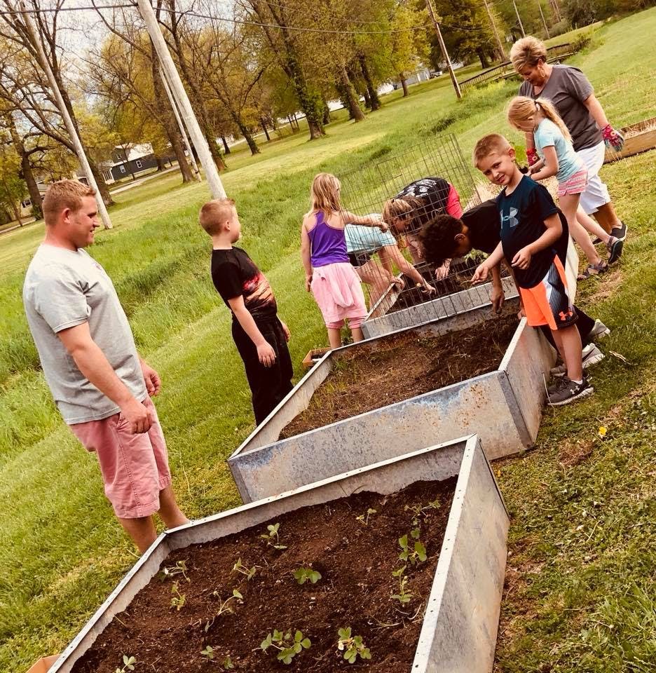 Adults and children planting in raised garden beds