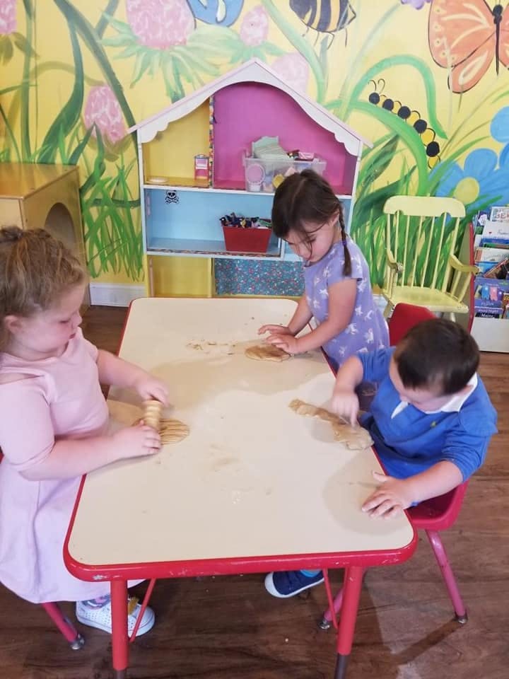 Three children playing with dough at a table in a classroom