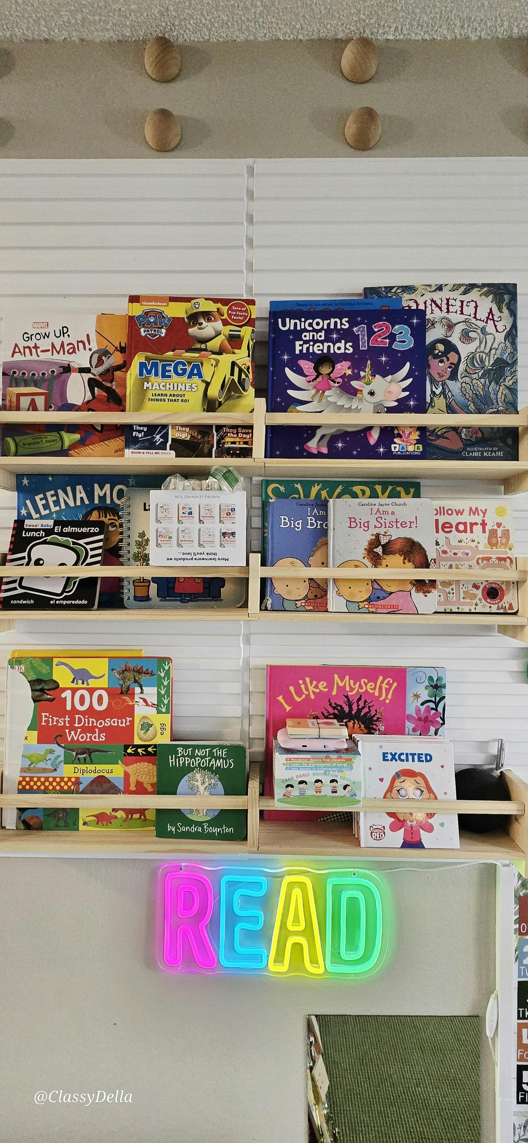 Wooden shelves filled with children's books above a colorful neon READ sign