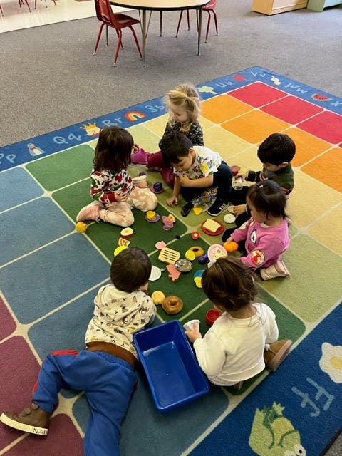 Children playing with toys on a colorful rug in a classroom