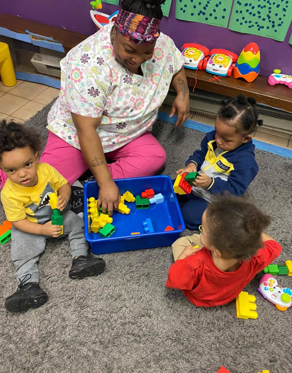 Adult and three children playing with building blocks on a rug