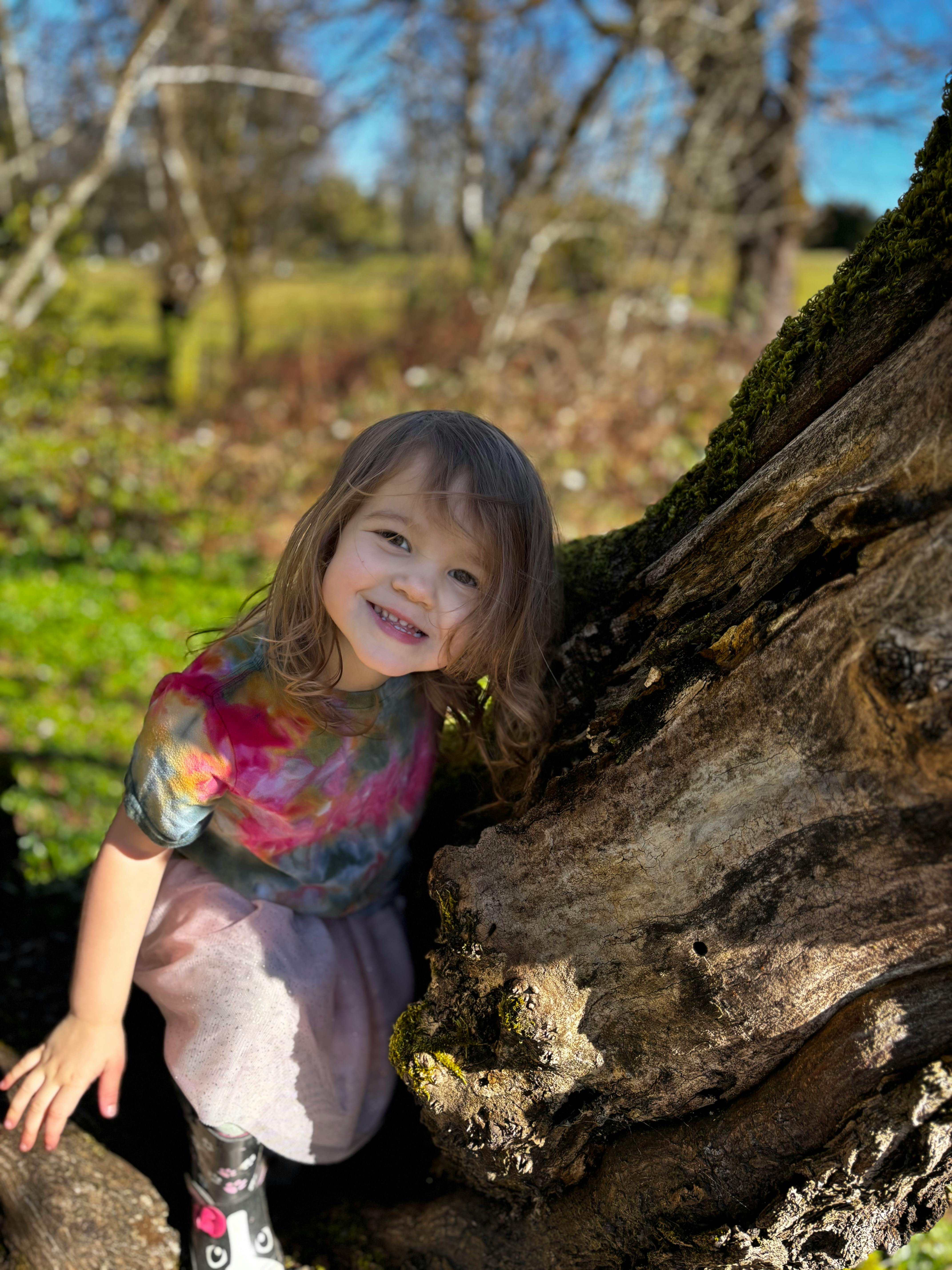 Child smiling next to a tree trunk