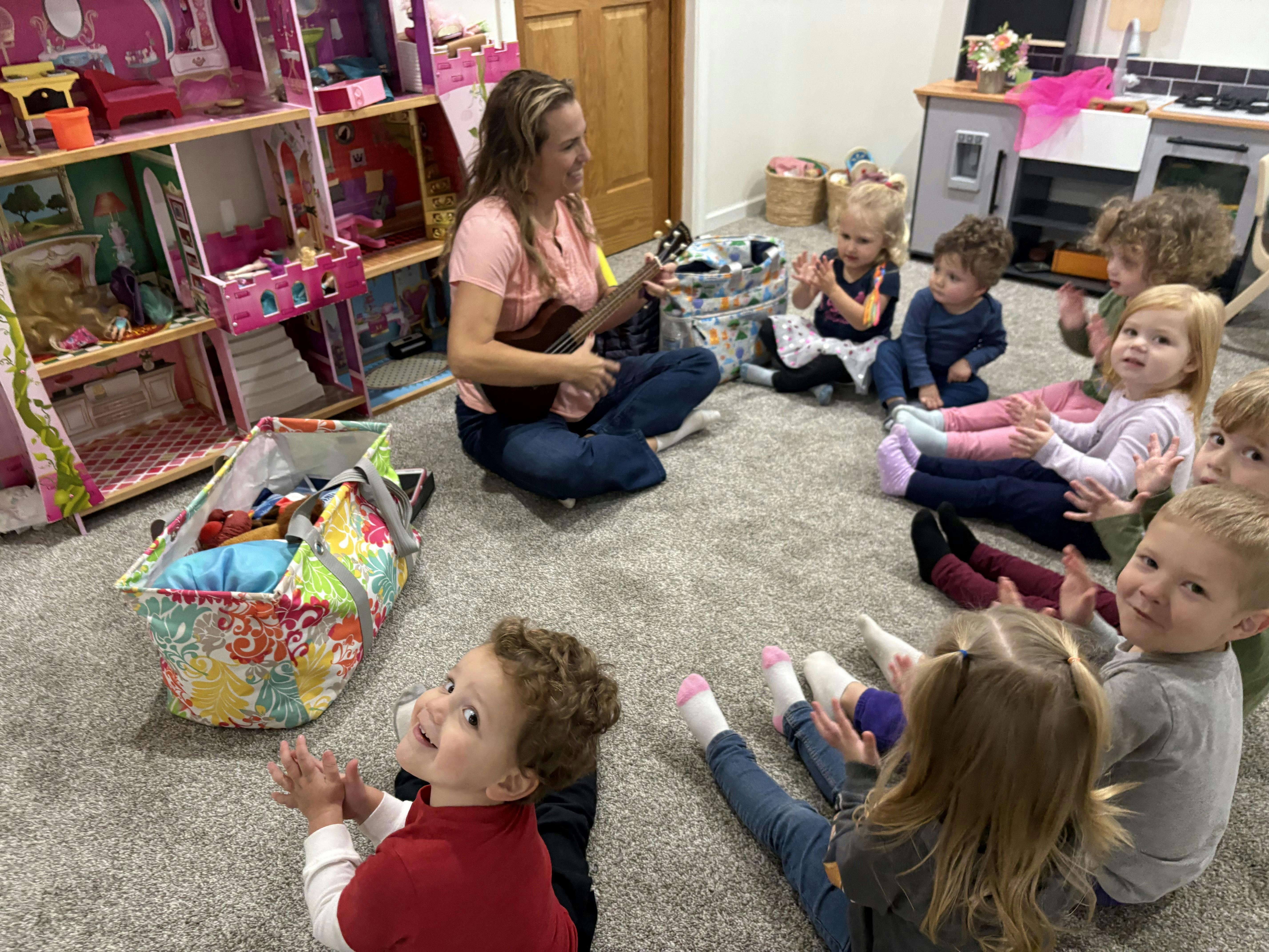 Person playing a ukulele for a group of children sitting children