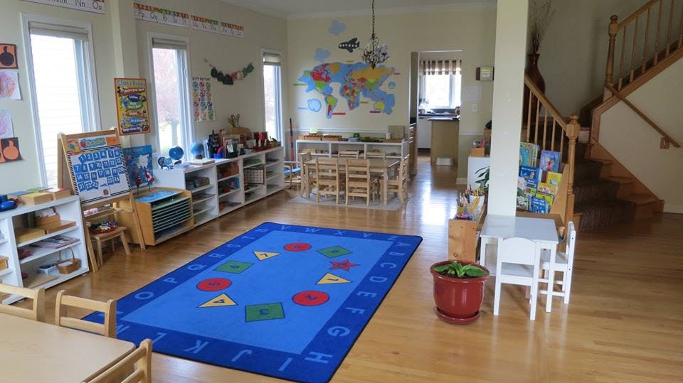 Classroom with a blue rug, small tables and chairs, and shelves with learning materials