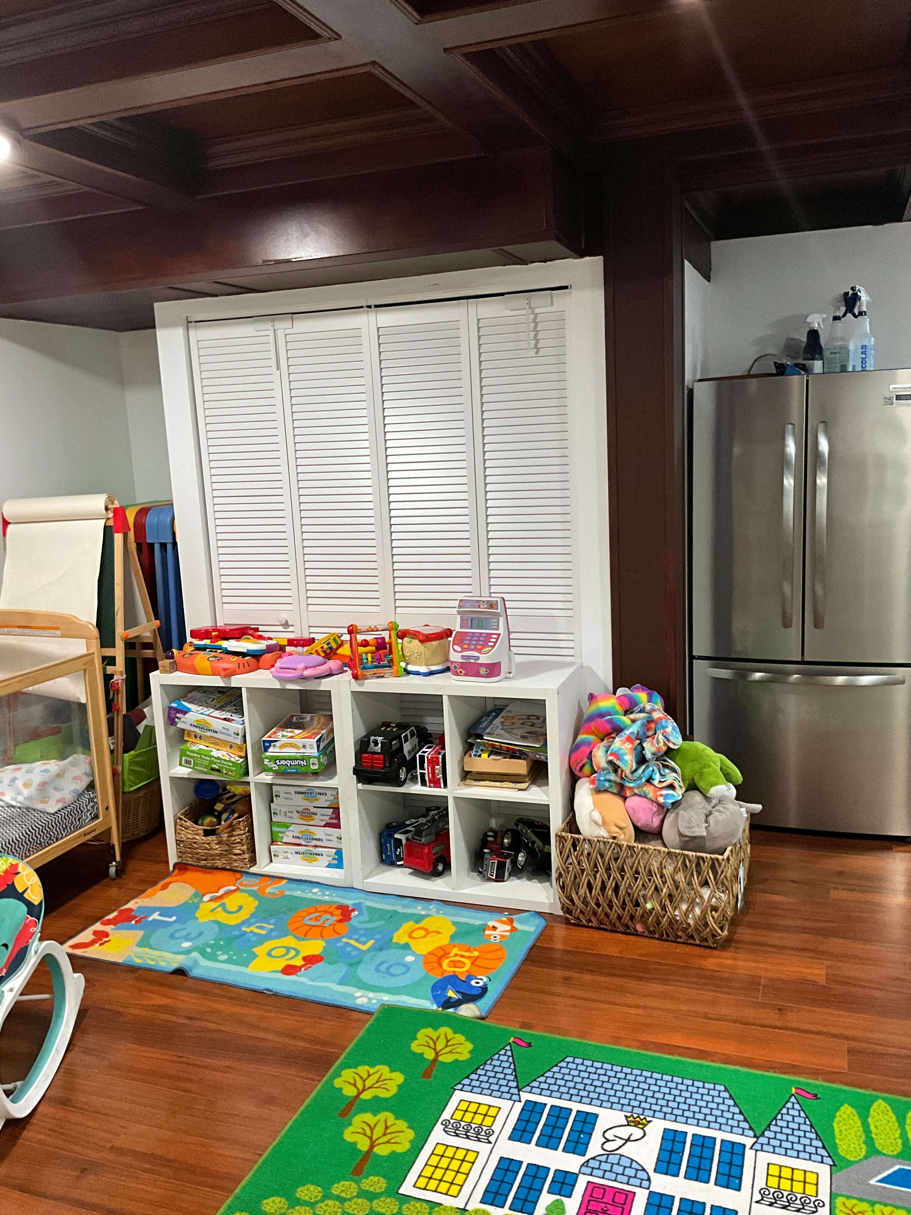 Playroom with white storage shelves, colorful rugs, and a stainless steel refrigerator