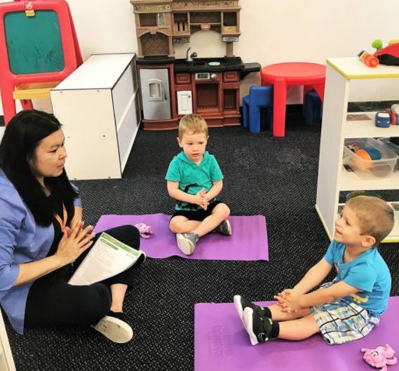 Person and two children sitting on mats in a classroom
