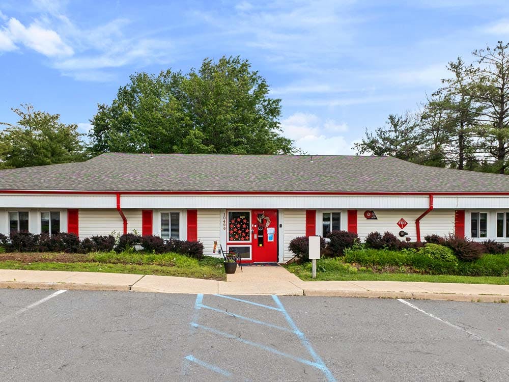 Single story building with white siding, red trim, and a red front door