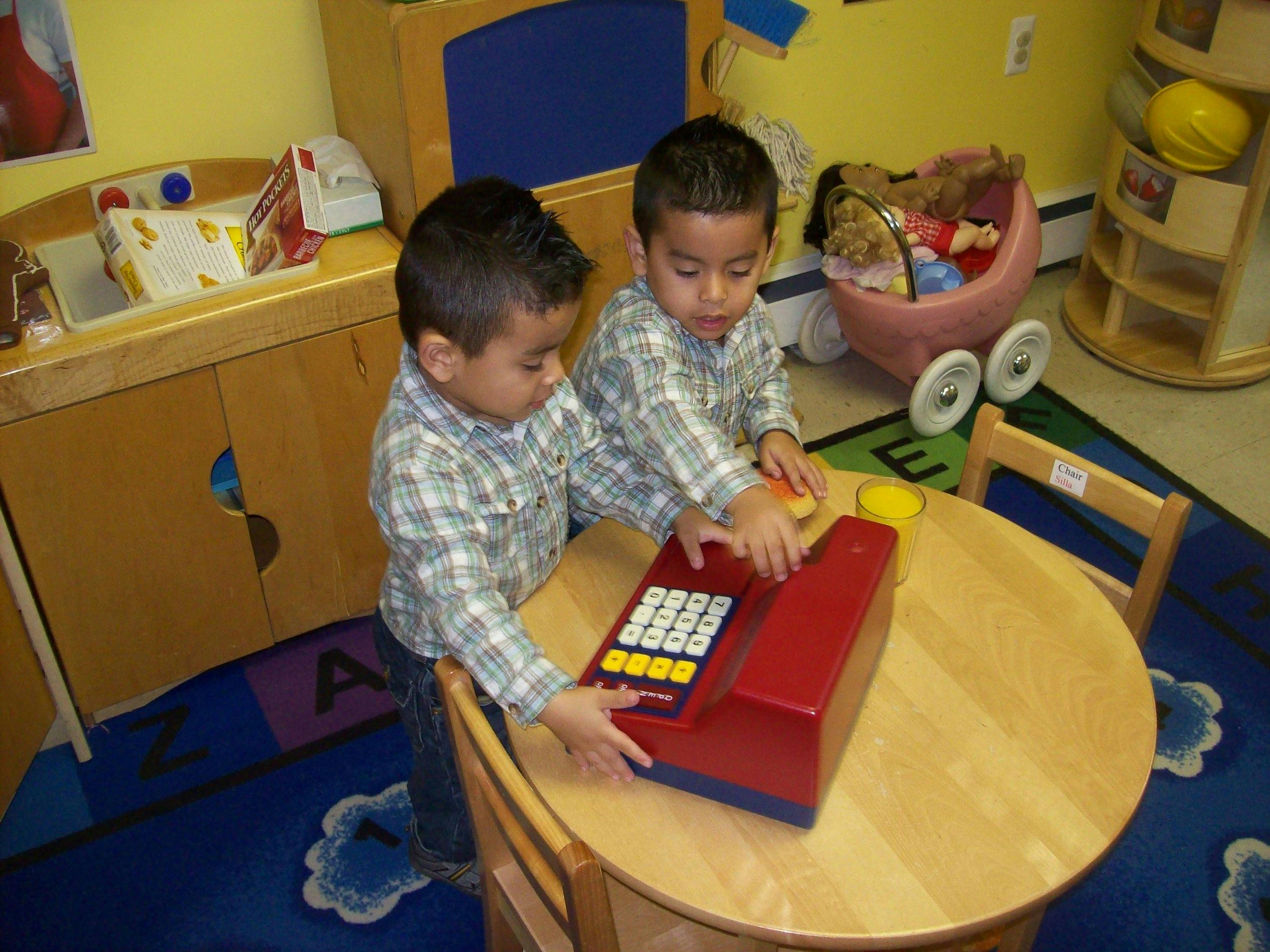 Two children playing with a toy cash register at a table