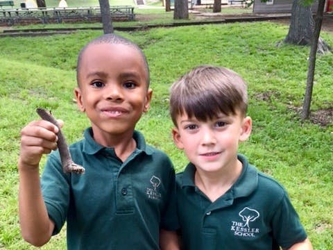 Two children in green shirts standing outdoors, one holding a stick