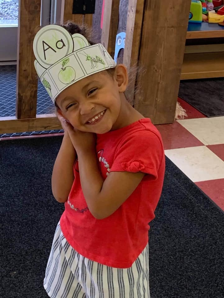 Child wearing a paper crown with the letter A and an apple