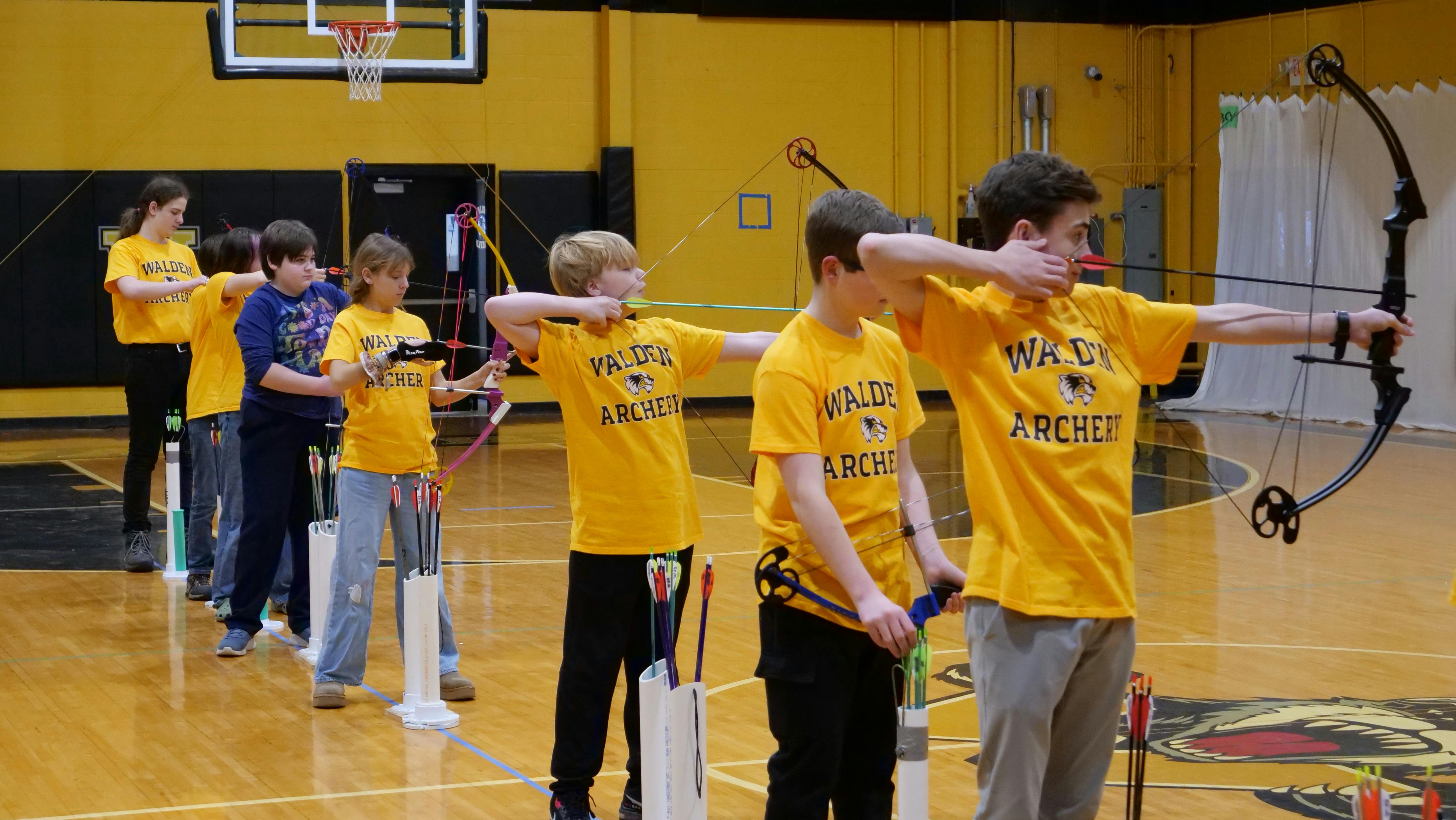 Group of teens and children with bows and arrows during archery practice in a gym