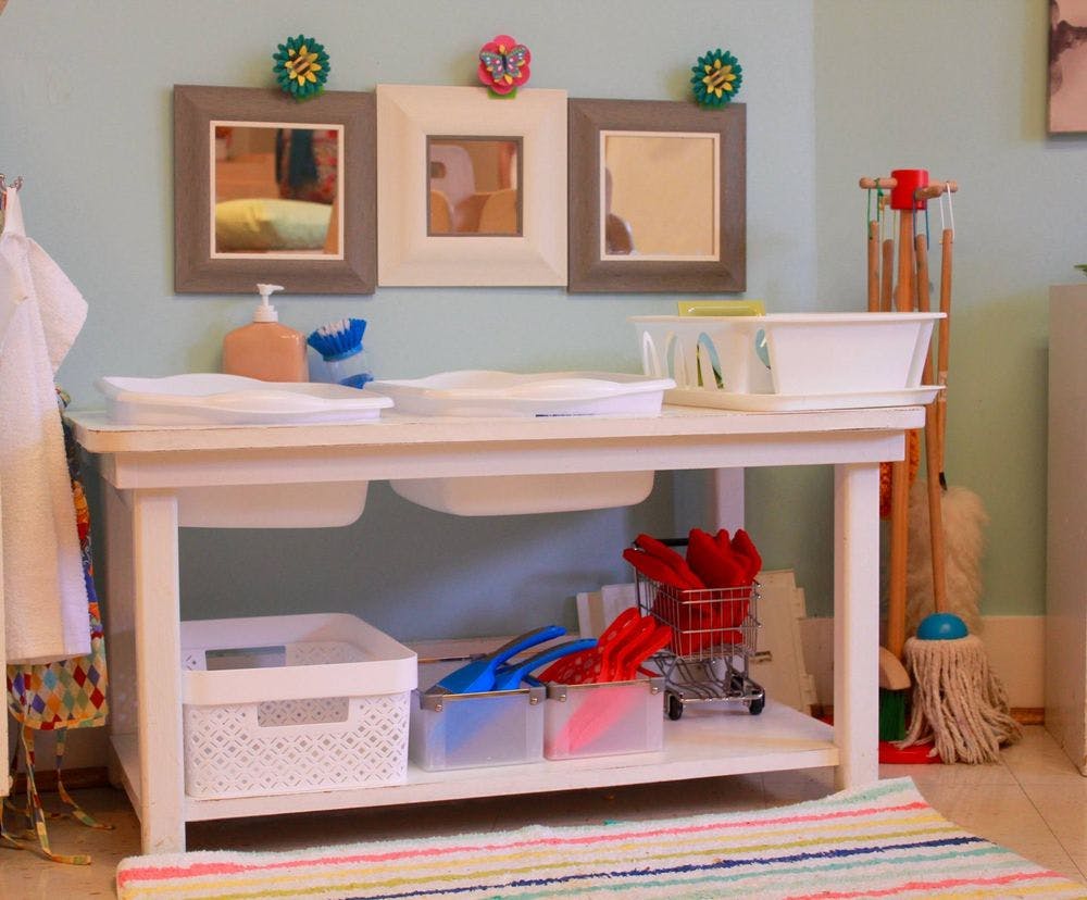 Child-sized cleaning station with a table, basins, and cleaning supplies