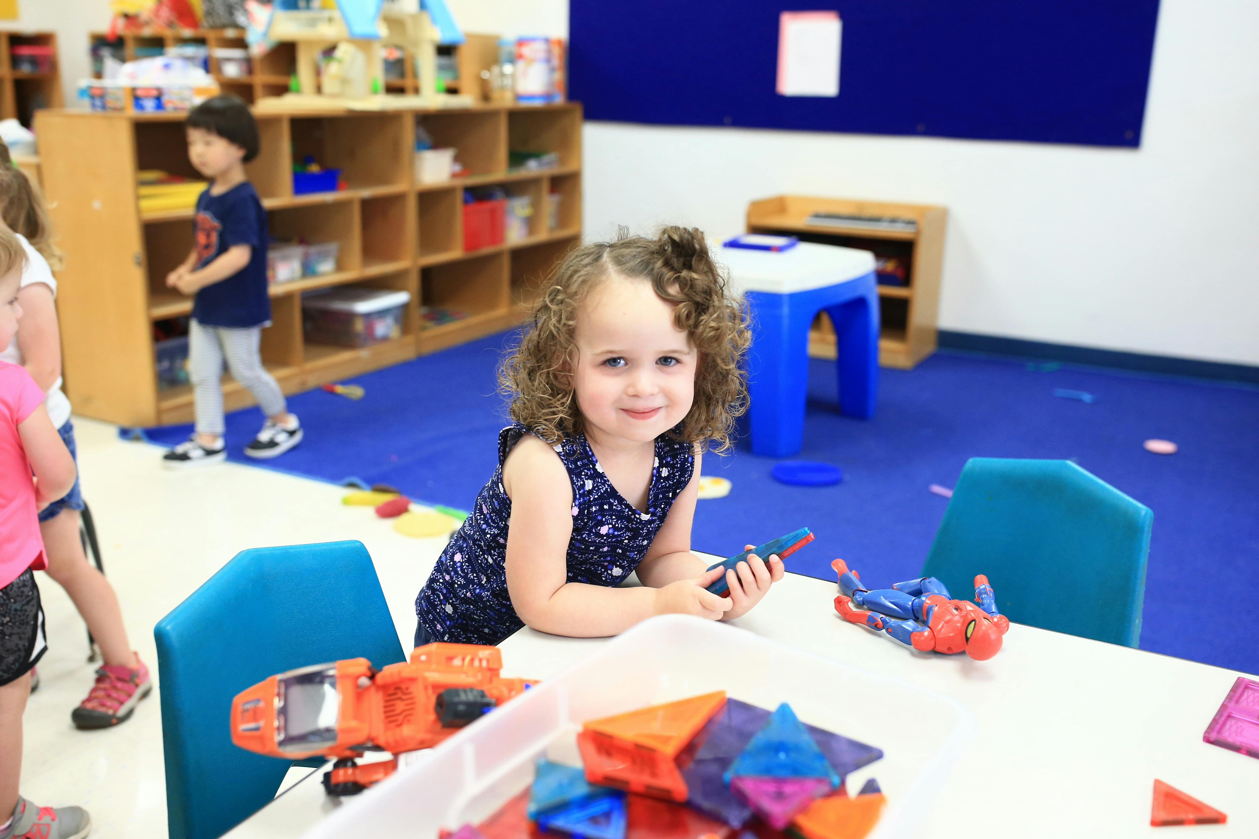 Child sitting at a table with toys, holding a toy
