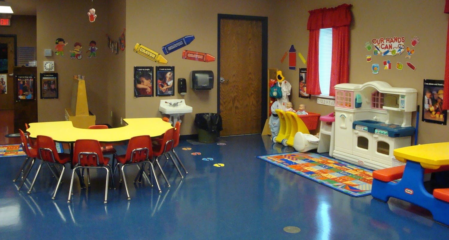 Classroom with small tables and chairs, play kitchen, and colorful rug