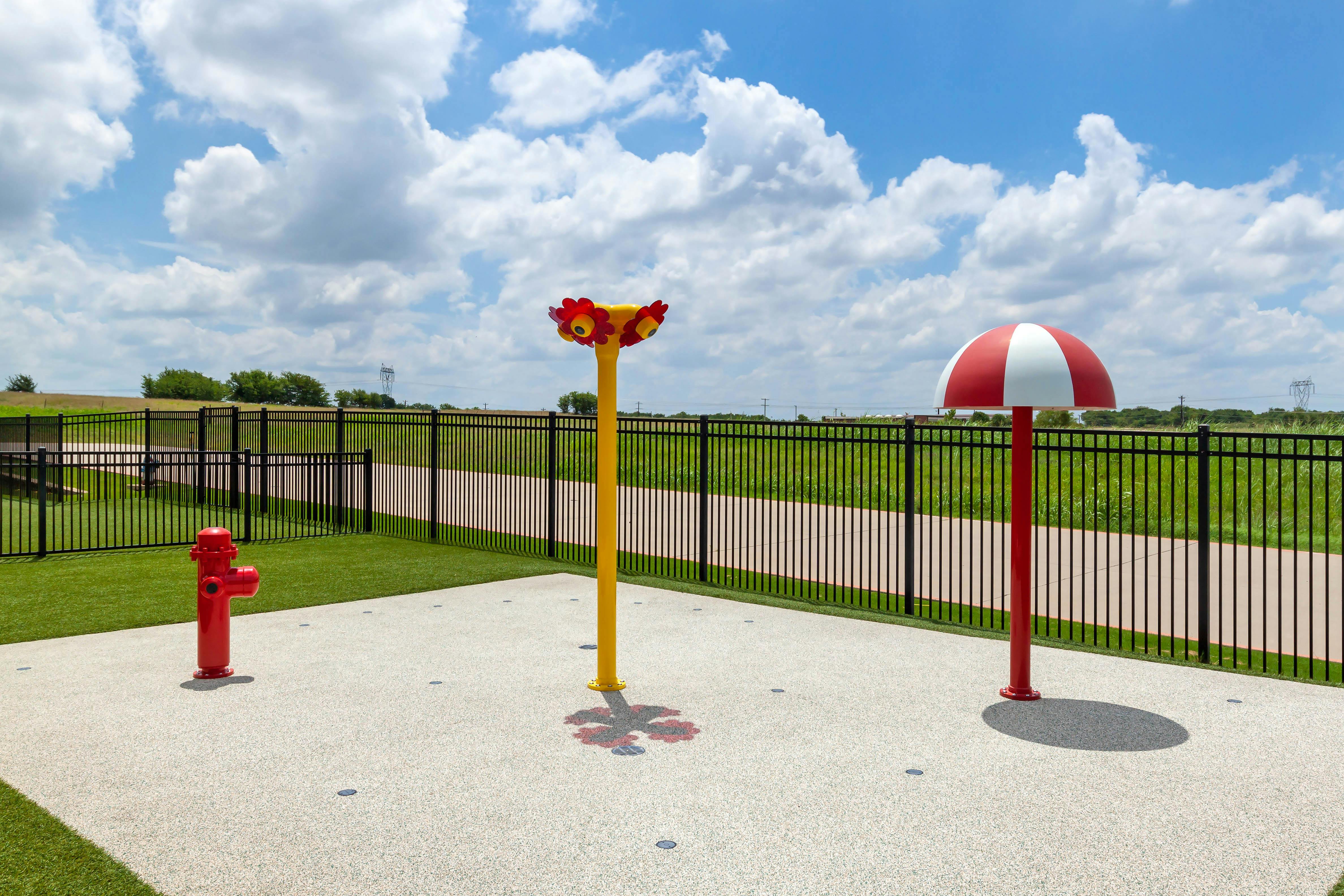 A splash pad with a red fire hydrant, a yellow flower-shaped sprinkler, and a red and white mushroom