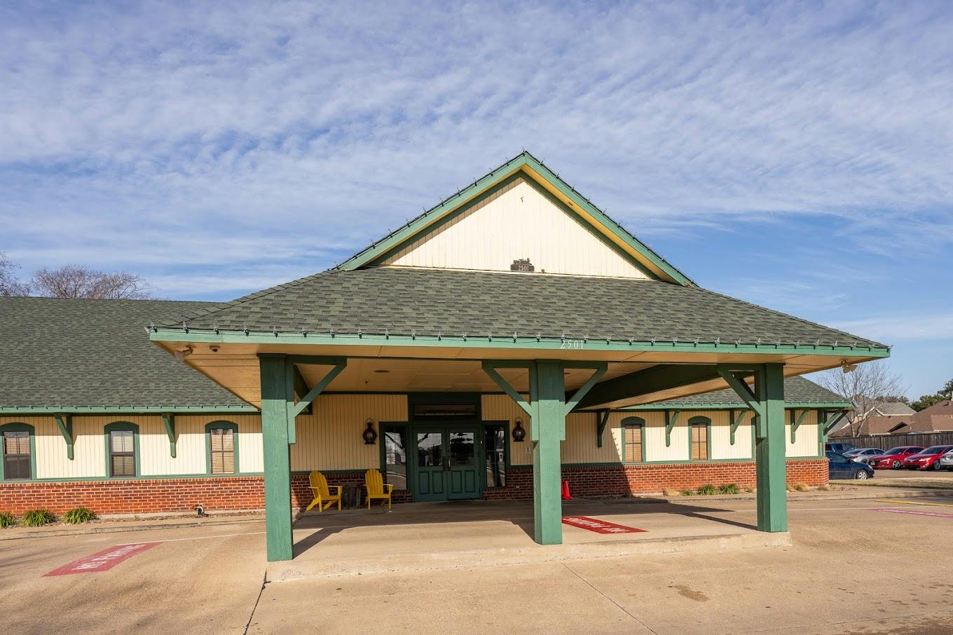 Single-story building with a large covered entrance and yellow chairs