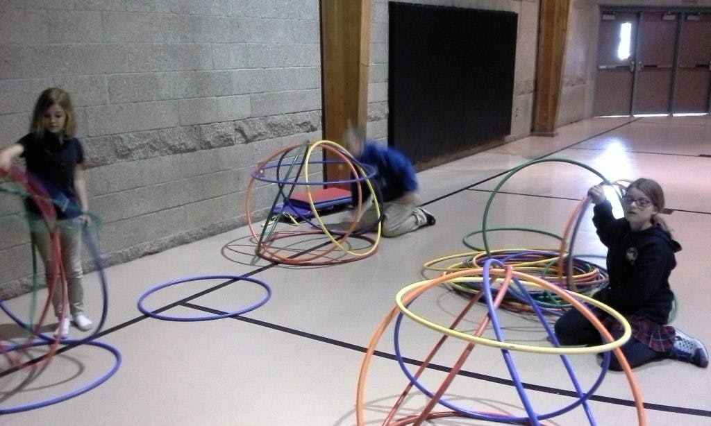 Three children playing with colorful hoops on a gym floor
