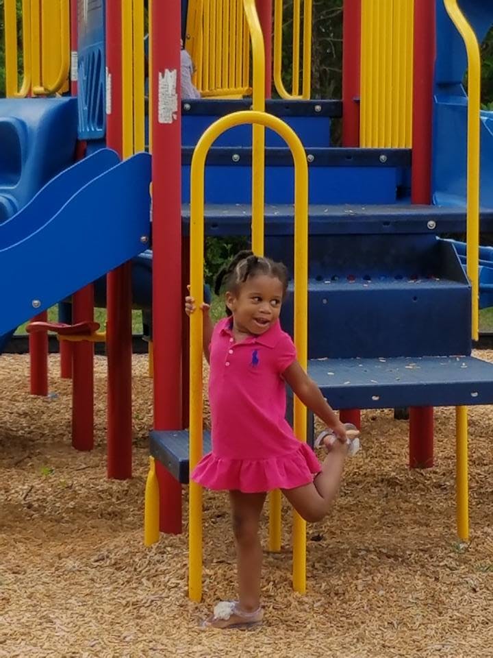 Child in a pink dress standing on a playground structure