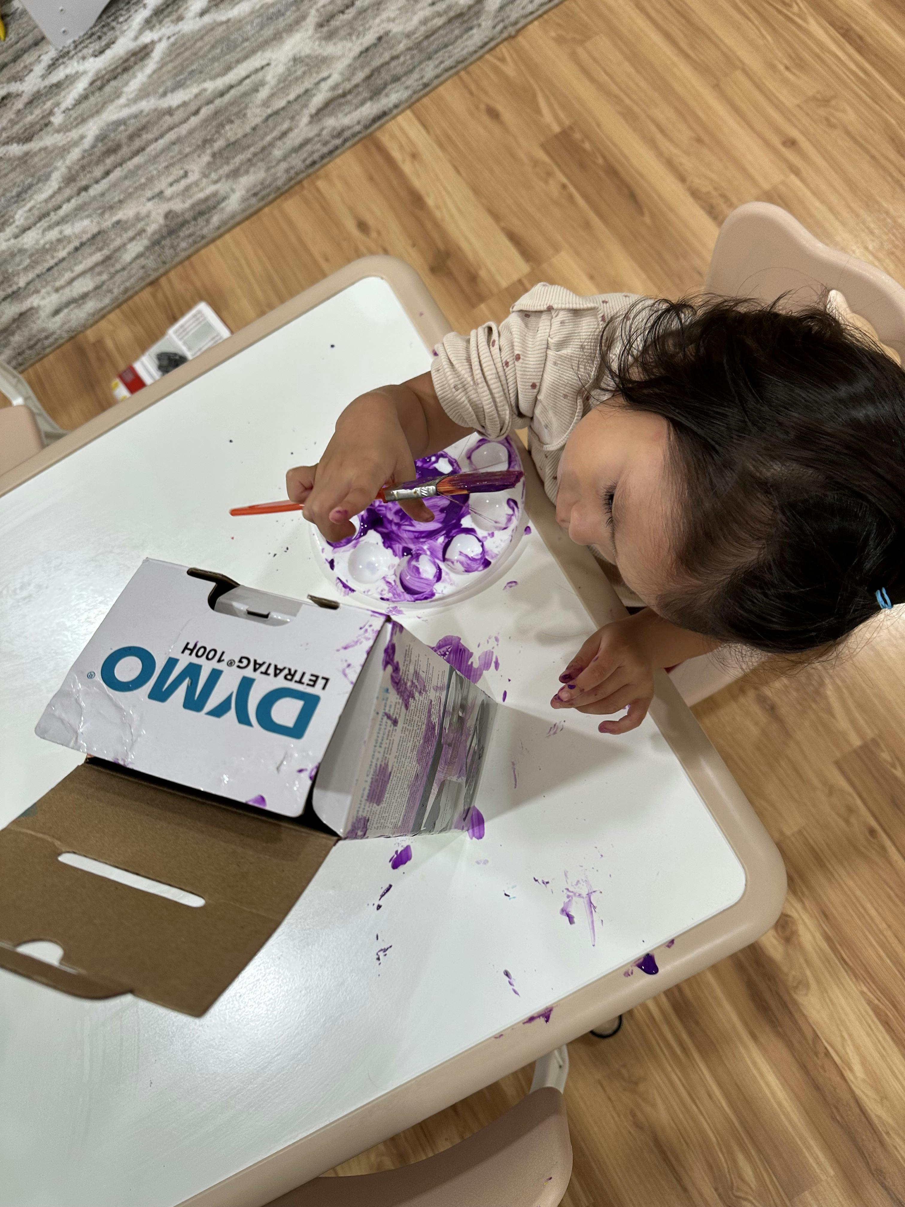Child painting with purple paint on a white table