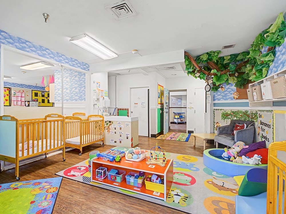 A colorful childcare room with cribs, play mats, and a tree decoration