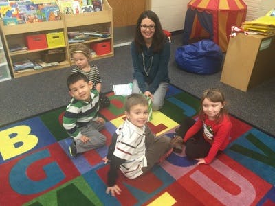 Adult and four children sitting on an alphabet rug in a classroom