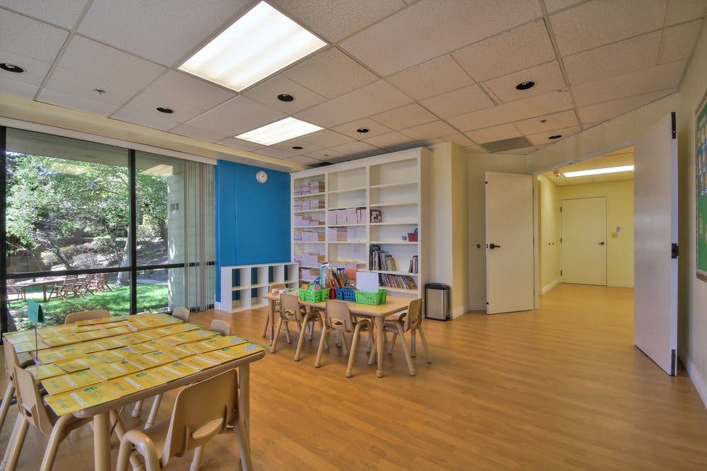 Classroom with small tables and chairs, bookshelves, and large windows