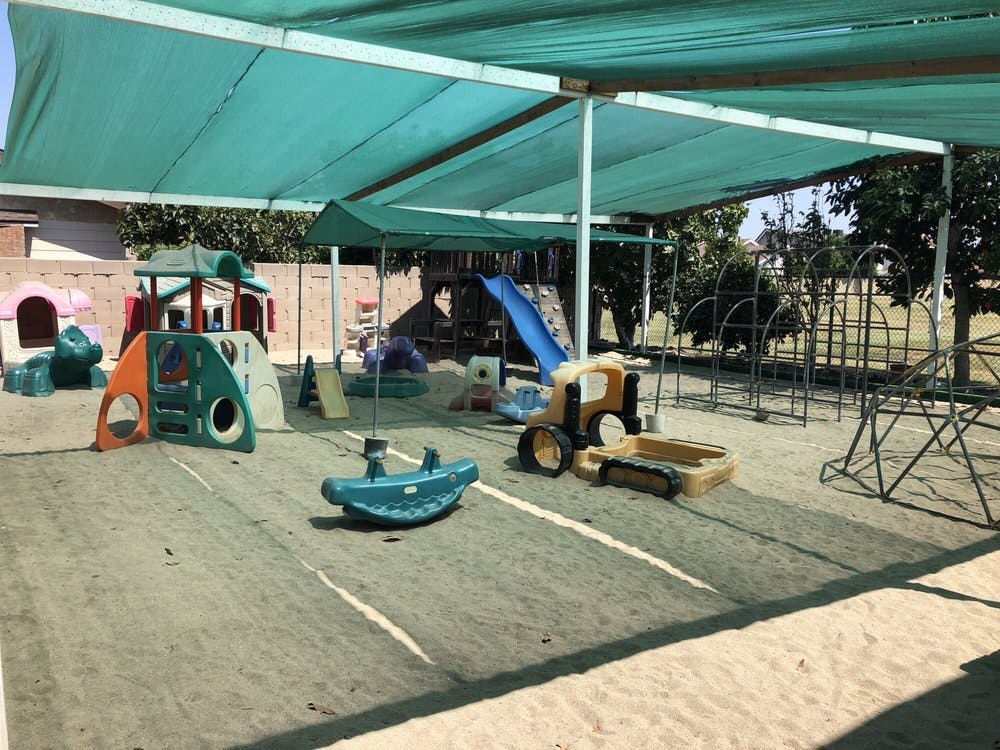 Outdoor playground with various play equipment under a green canopy