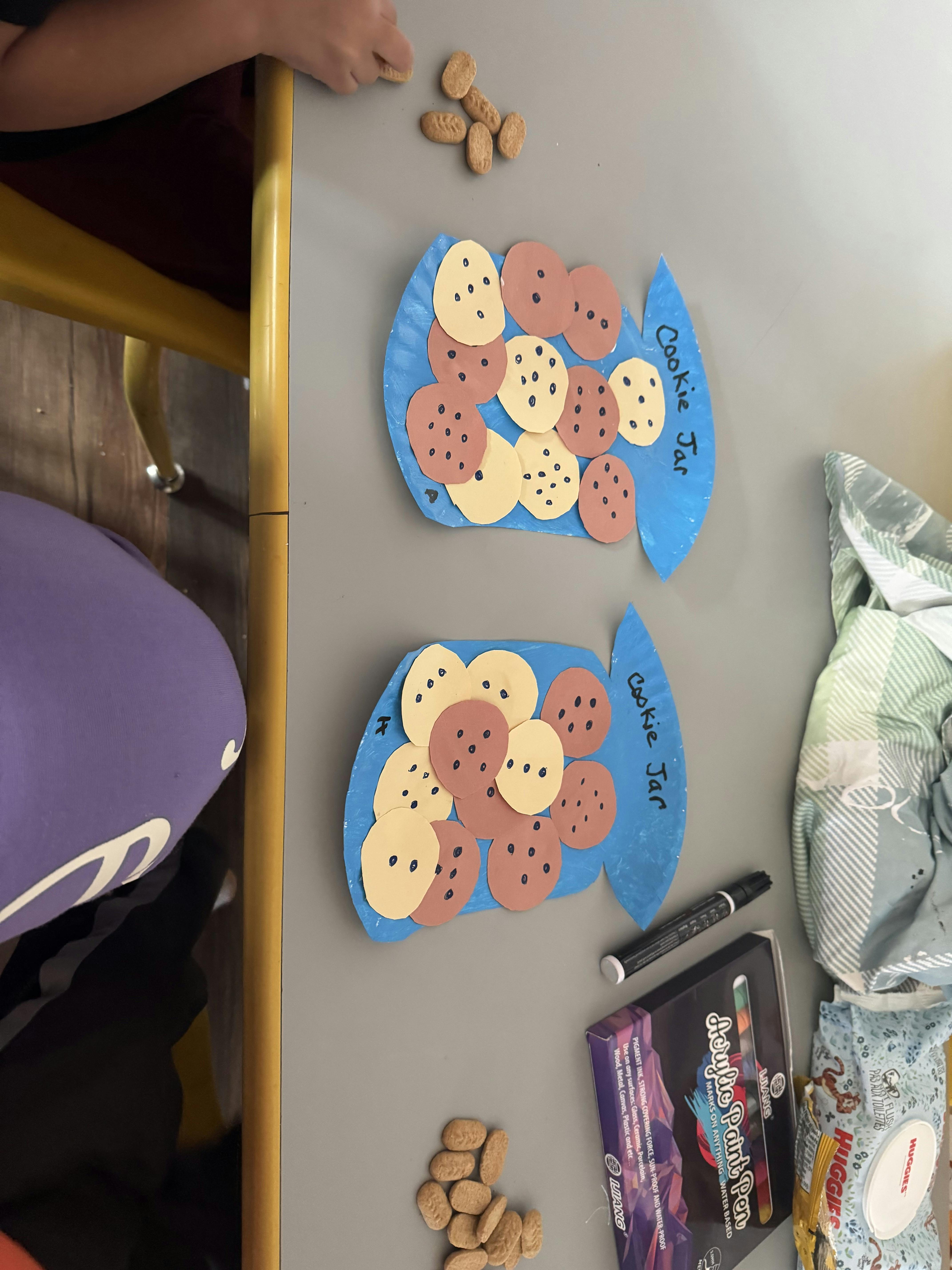 Child crafting paper cookie jars with paper cookies on a table