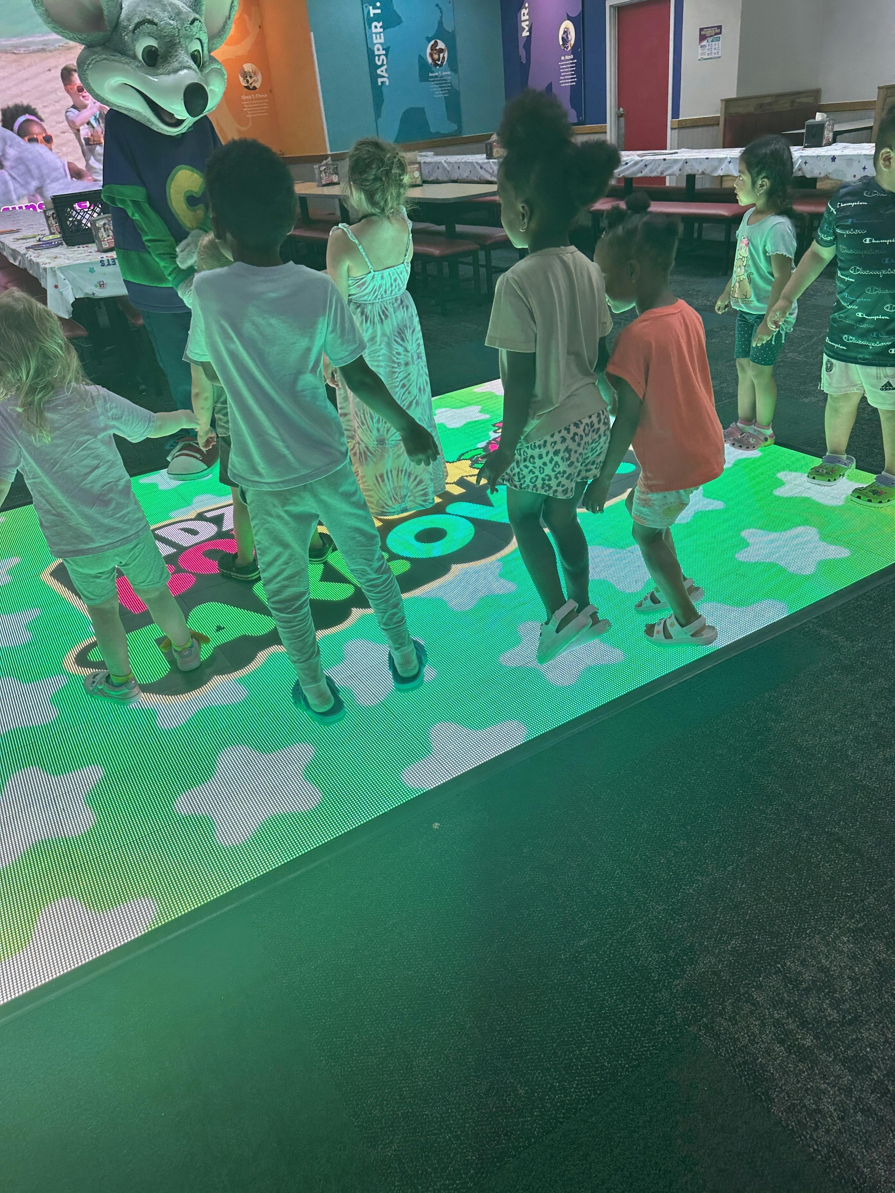 Children dancing on an interactive light-up floor with a costumed character