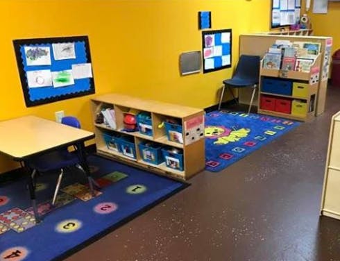 Classroom with yellow walls, blue rugs, small table, and shelves with shelves