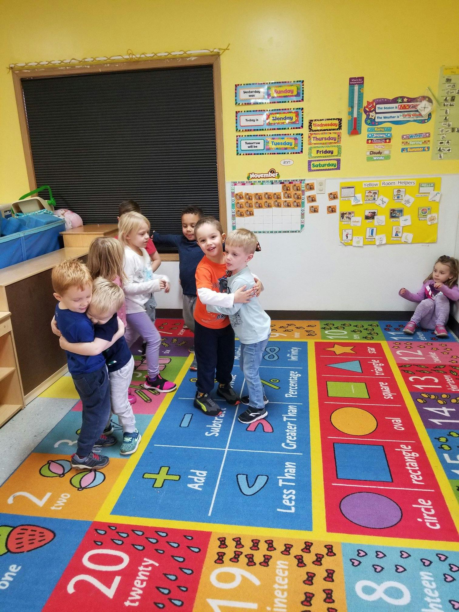 Children standing on a colorful rug with numbers and shapes