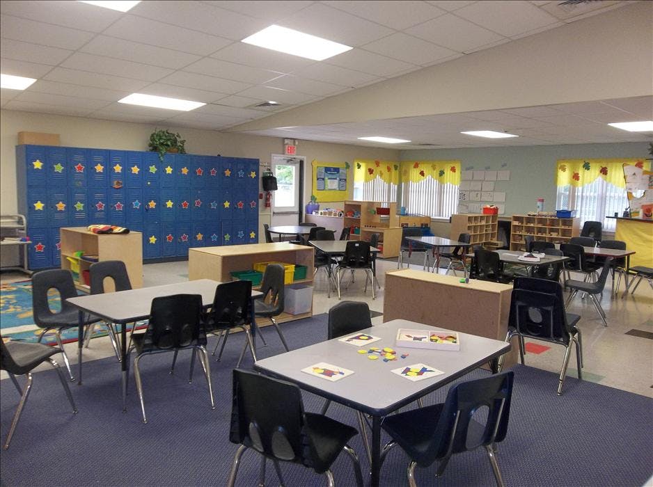 An empty classroom with small tables and chairs, and blue lockers with stars