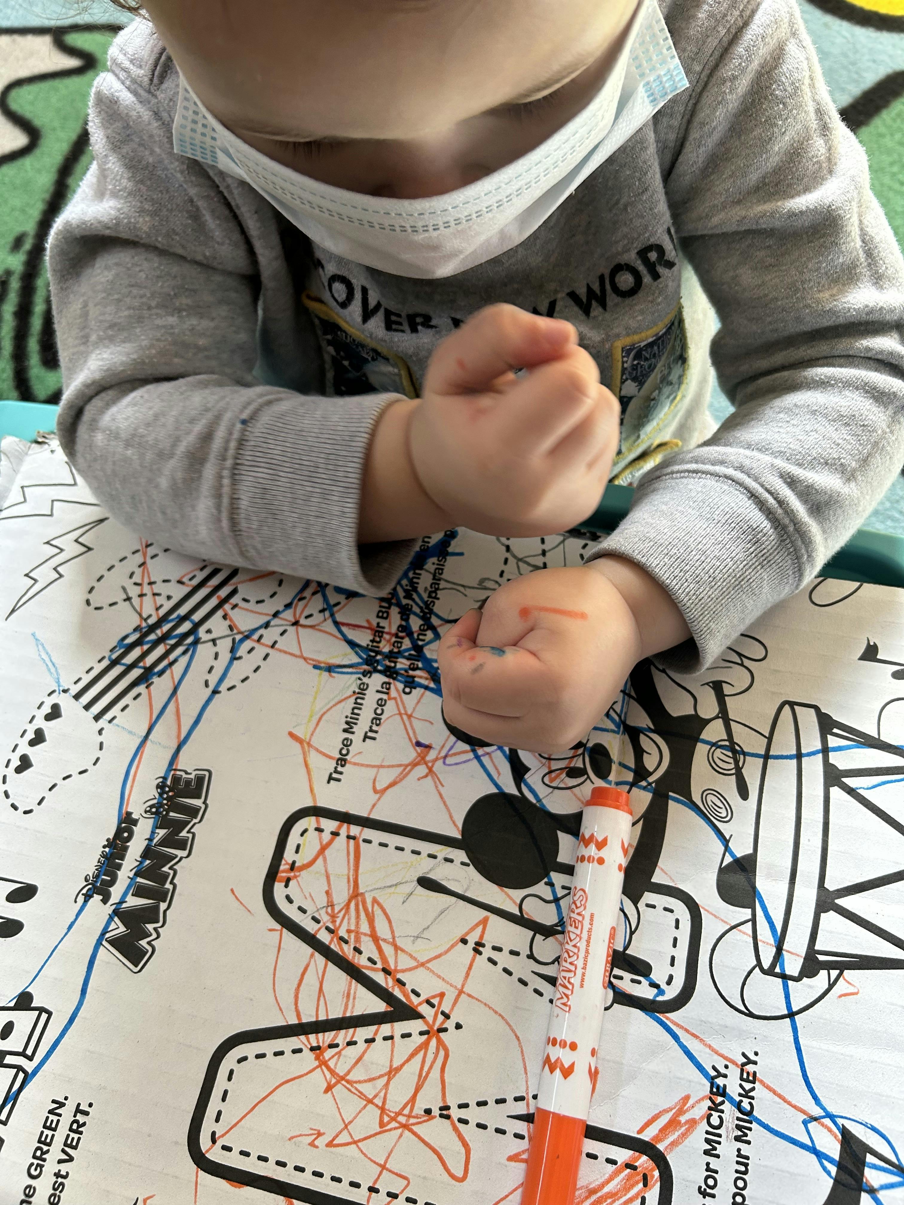 Child in a face mask coloring a Minnie Mouse tracing sheet with markers