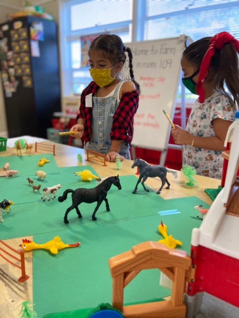 Two children in masks playing with farm animal toys