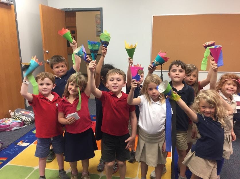 Children holding up colorful crafts in a classroom