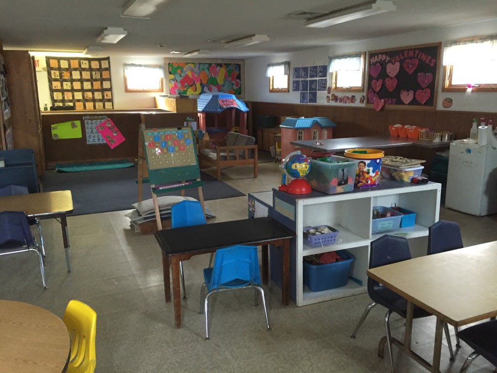 Classroom with small tables and chairs, shelves with toys, and artwork on walls