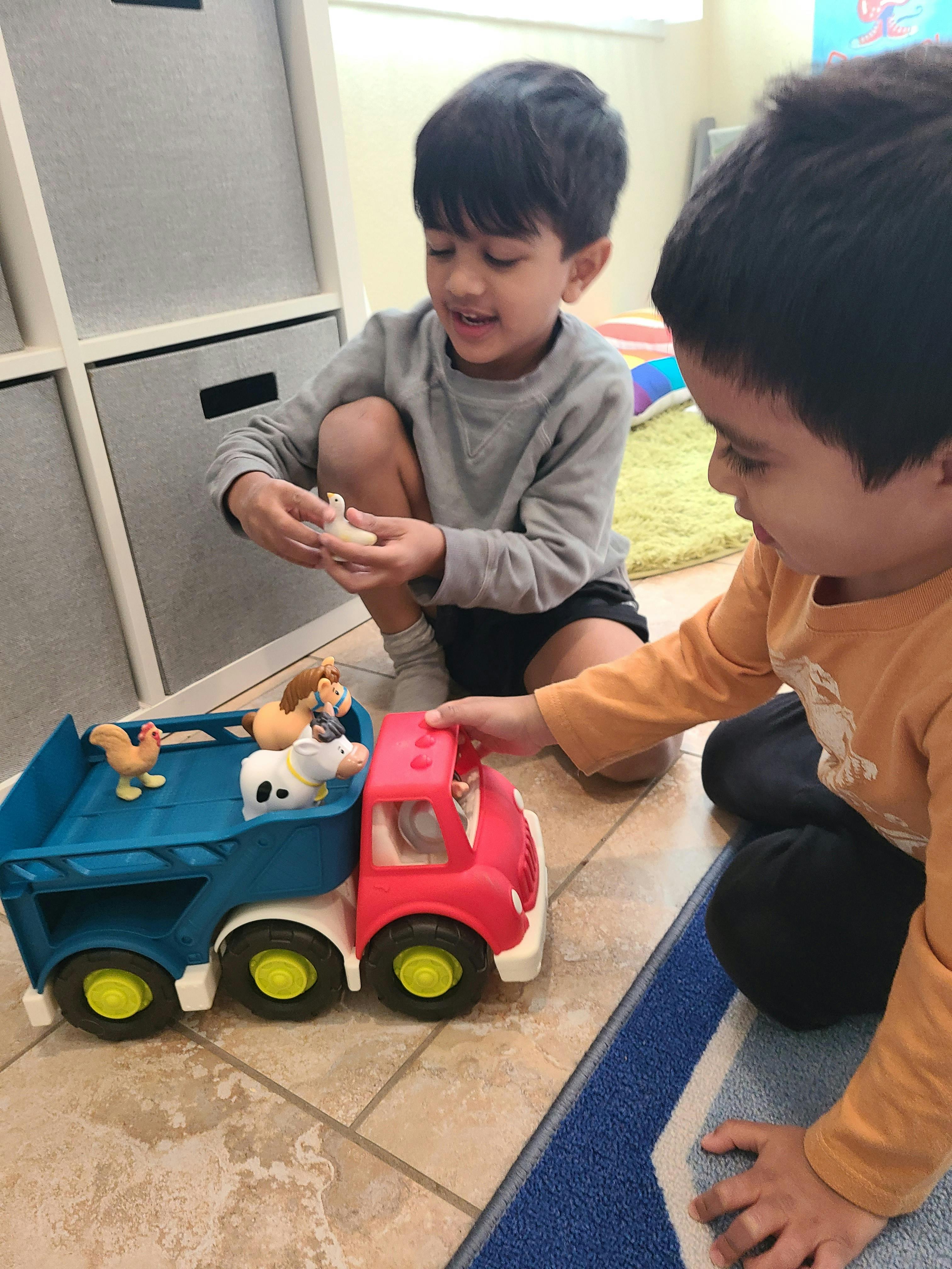 Two children playing with a toy truck and animal figures