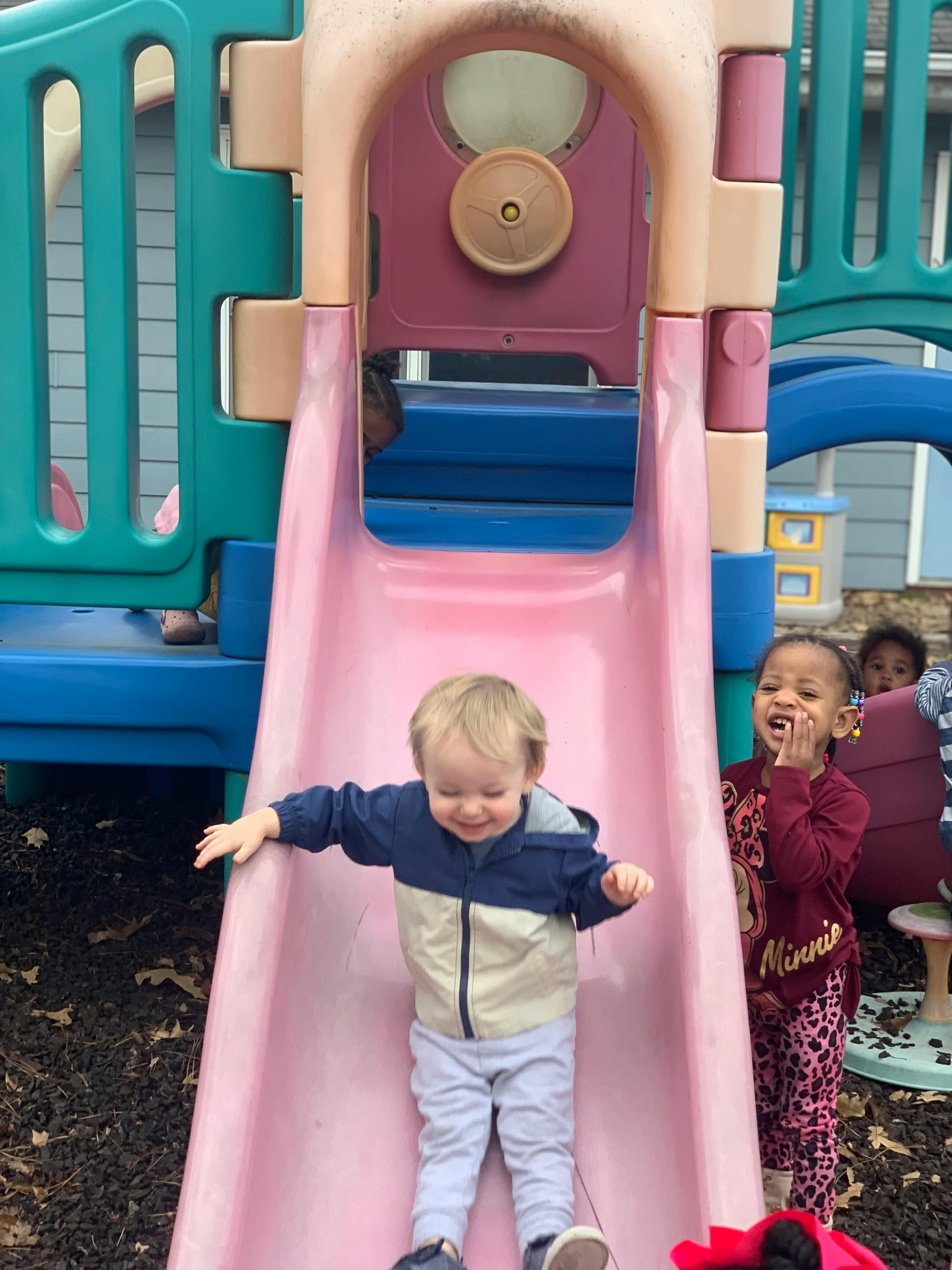 Child sliding down a pink slide on a playground