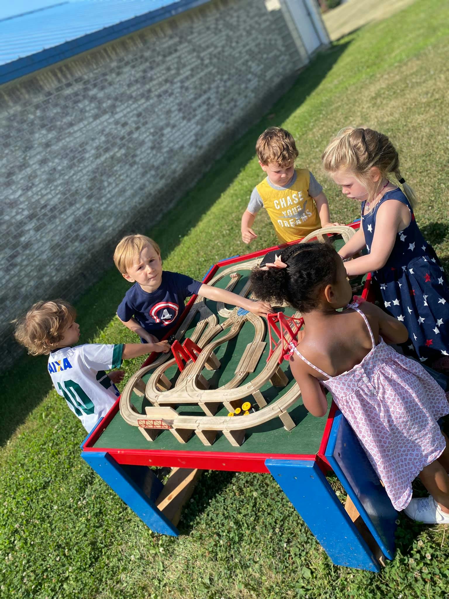 Children playing with a train set on a table outdoors