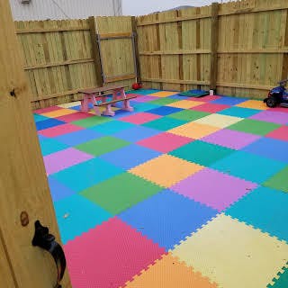 Outdoor play area with colorful interlocking foam tiles and a wooden fence