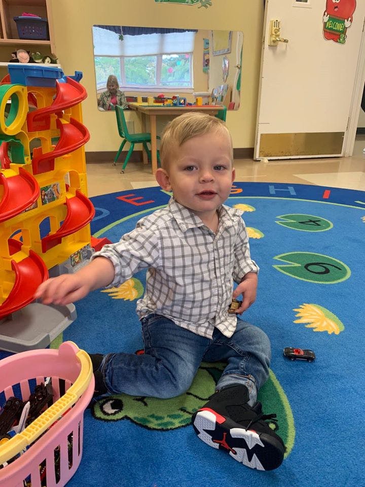 Child sitting on a blue rug with toys in a room with toys