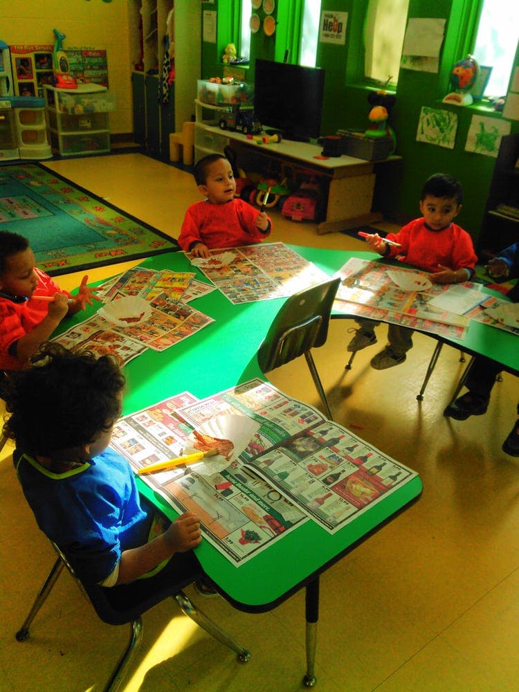 Children sitting at green tables with papers in a classroom