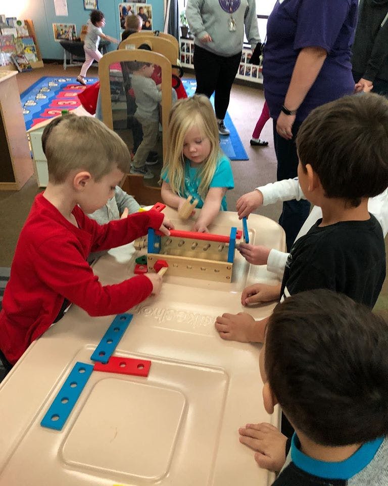 Children playing with a wooden toy on a table in a classroom