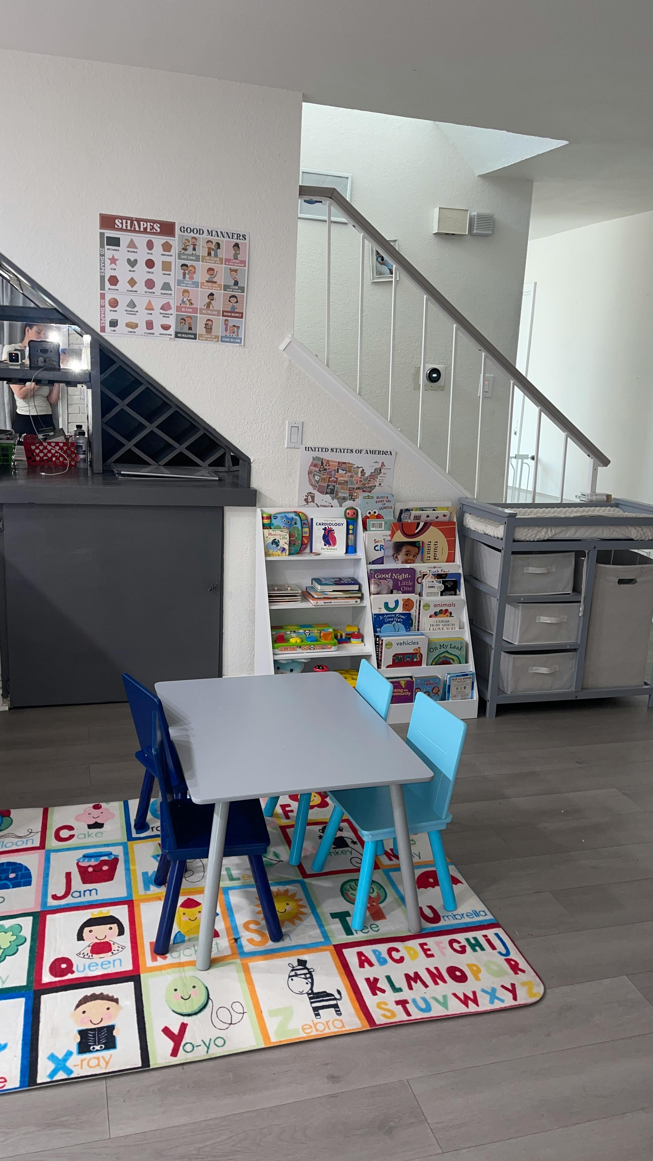 Children's table and chairs on an alphabet rug in a room with shelves