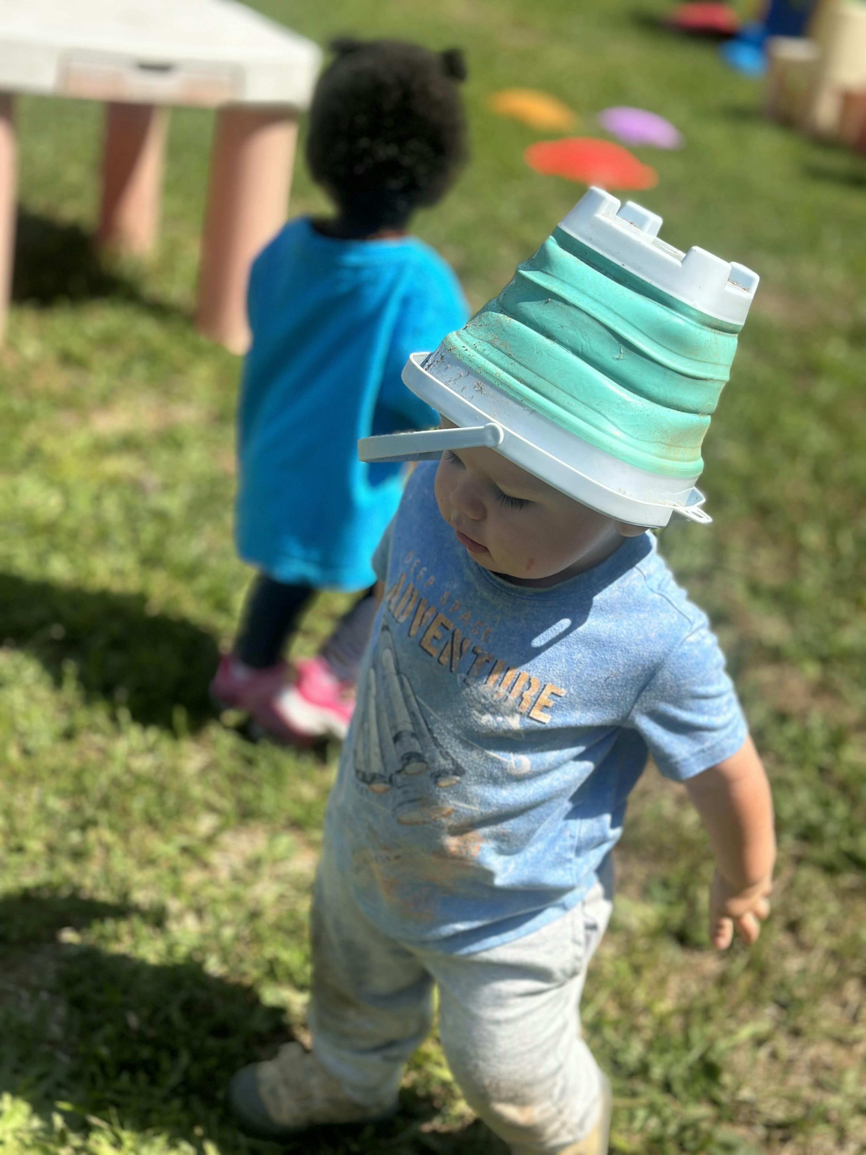Child with a green bucket on their head, another child in background