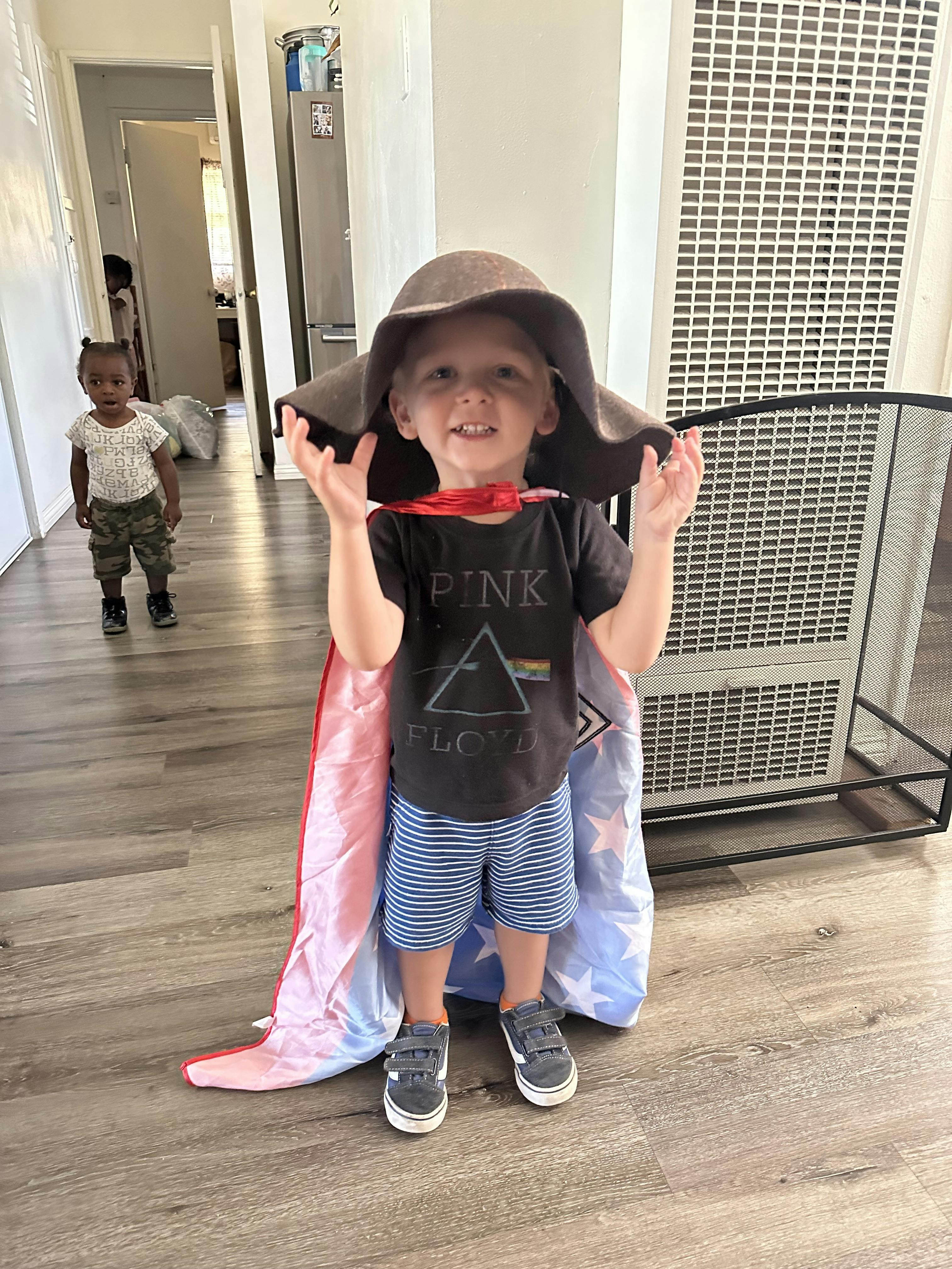Child in a large hat and cape with another child in the background