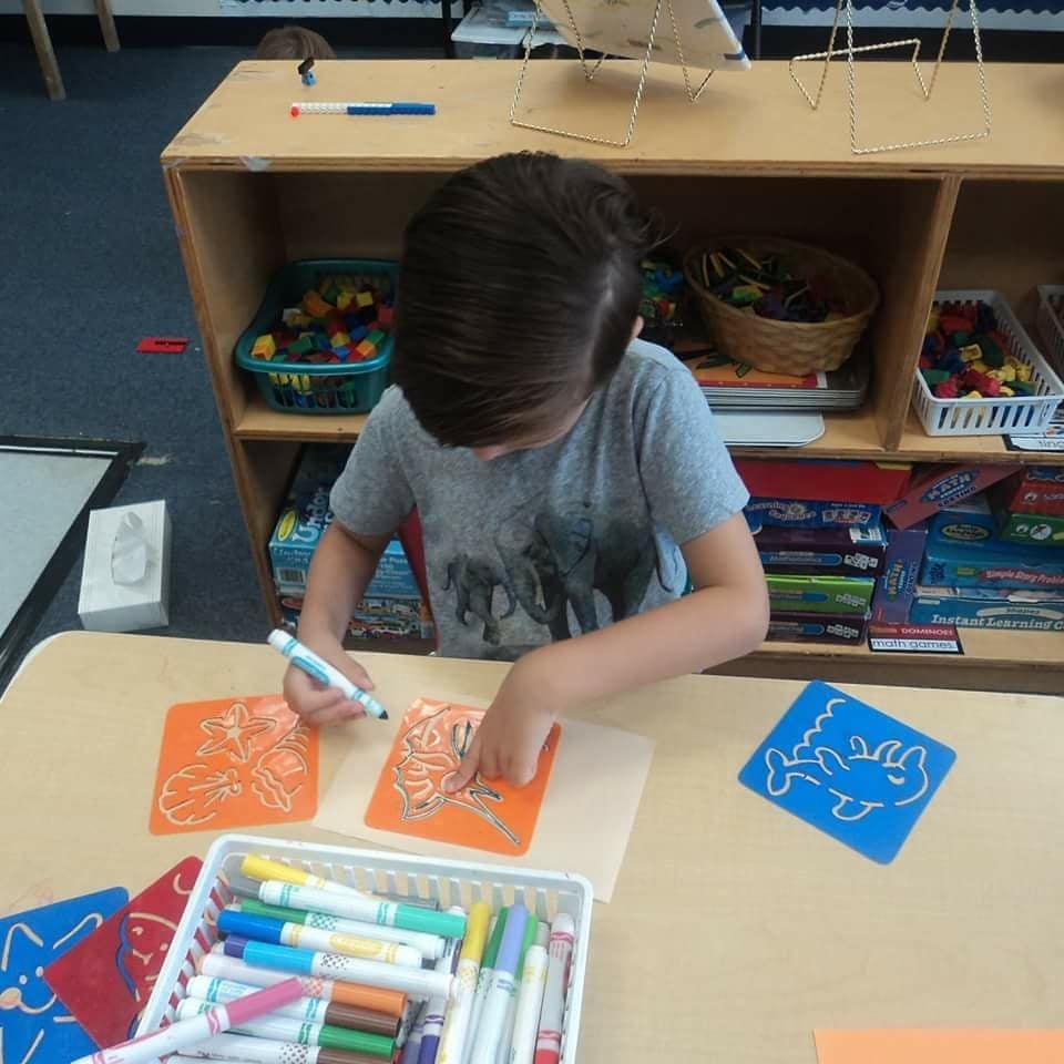 Child drawing on orange paper with a marker in a classroom